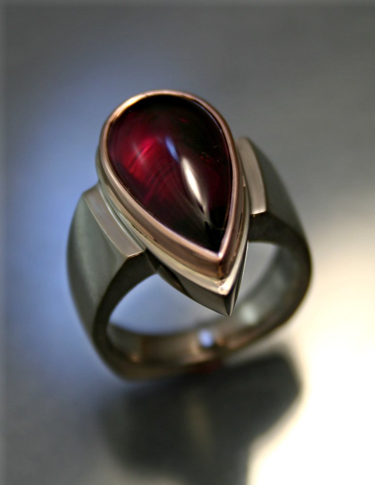 A silver ring with a maroon, teardrop-shaped gemstone.