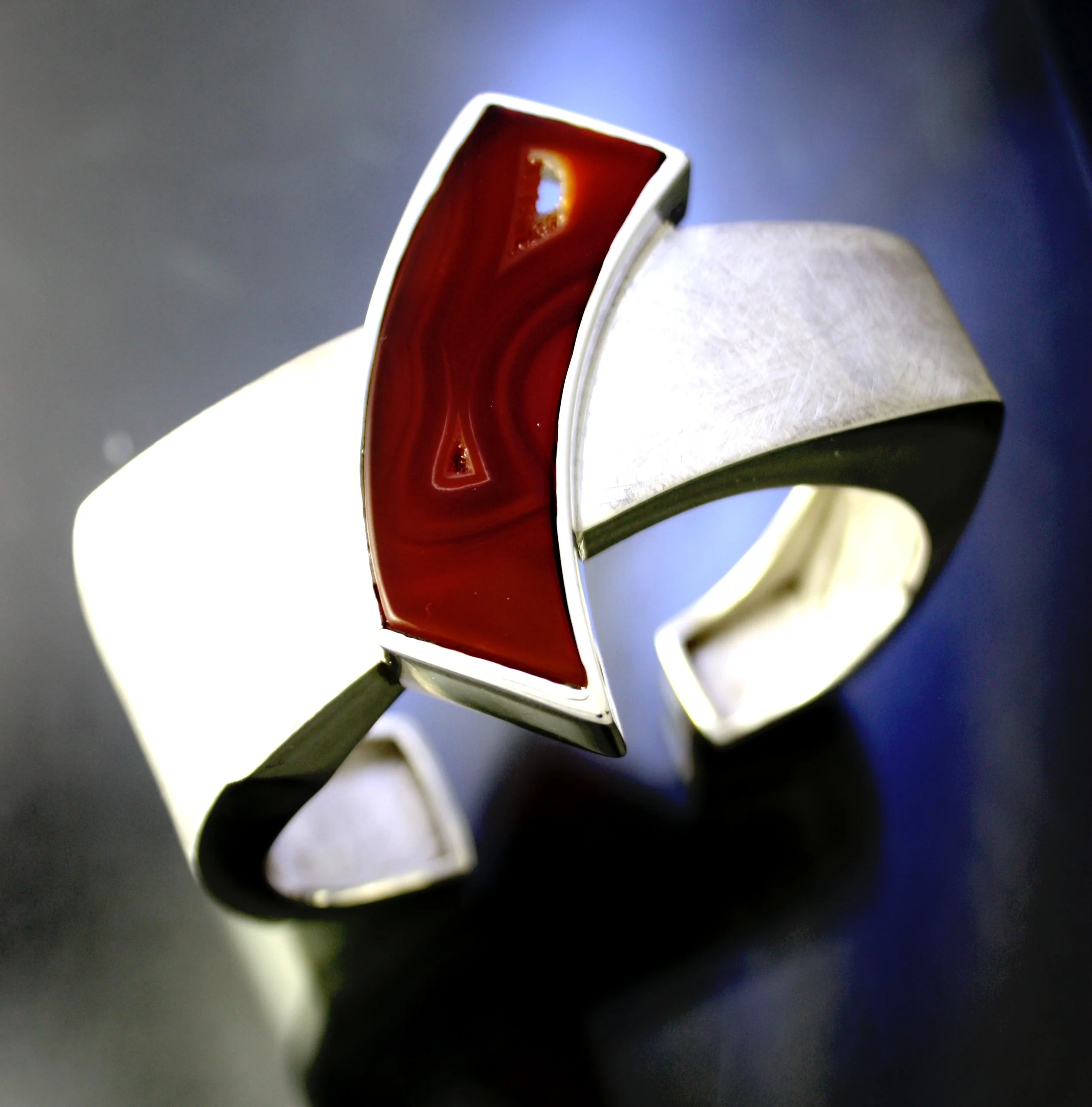 A modern silver ring featuring a rectangular red stone with marbled patterns.