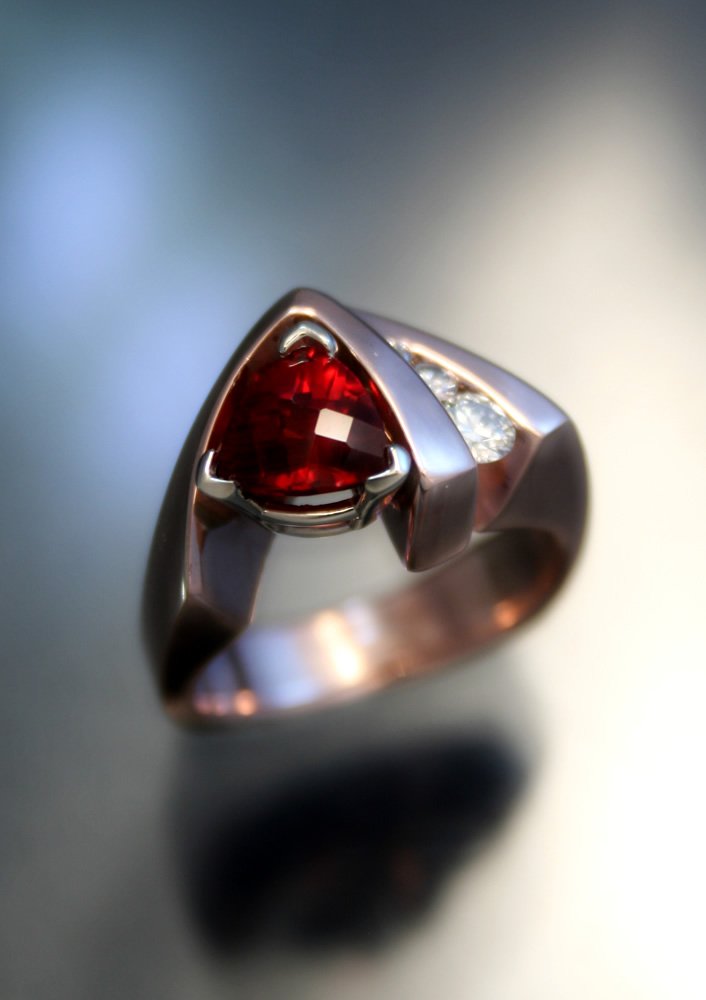 A silver ring with a heart-shaped red gemstone and small clear stones on the band.