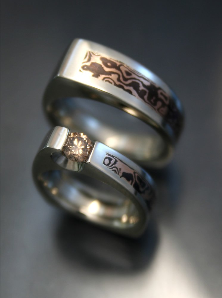 Close-up of two silver rings, one with a patterned design and the other with a small diamond set into it, on a dark surface.