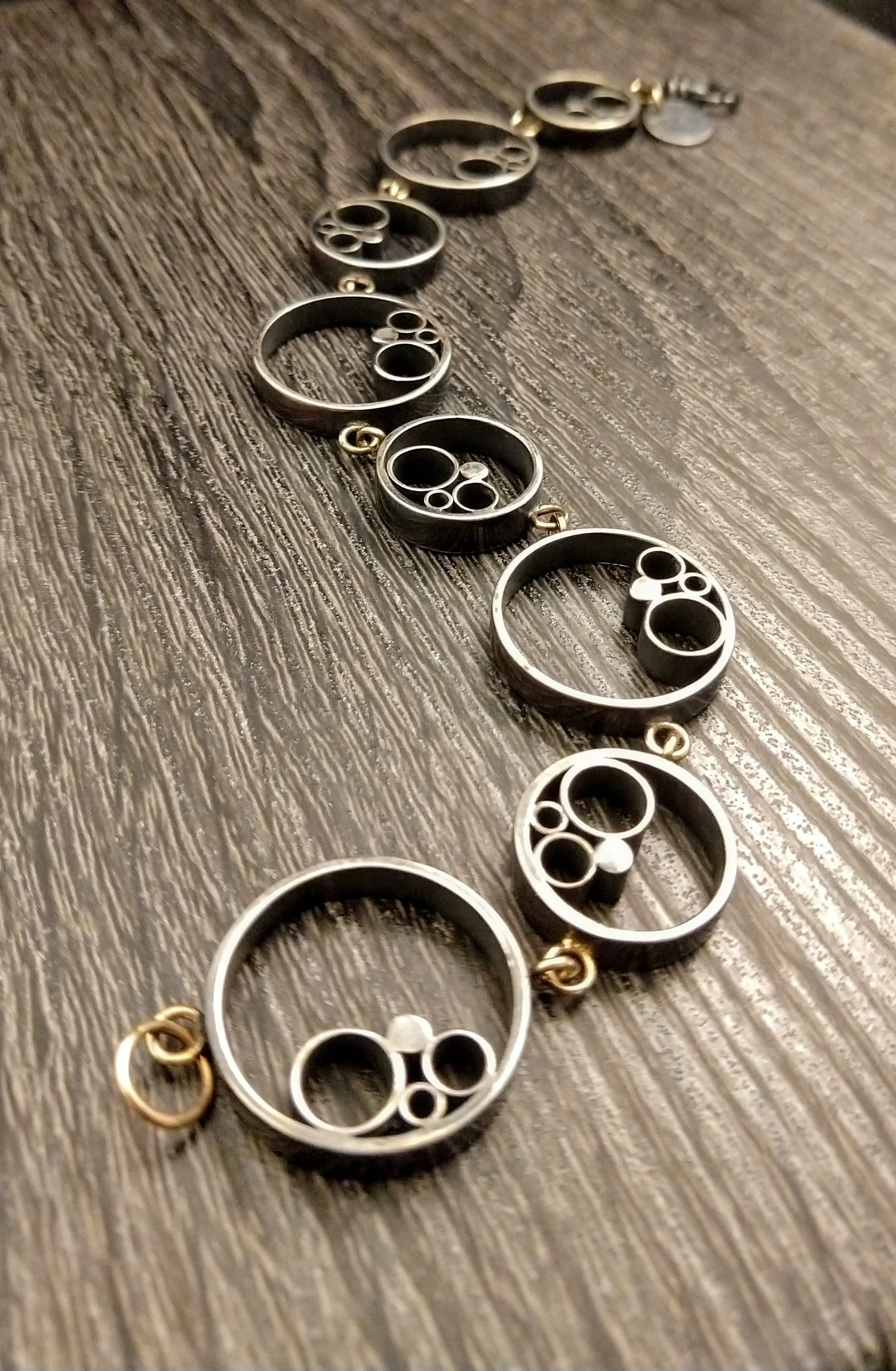 A long necklace made of circular metallic links, some with small spheres or smaller rings inside, laid out on a wooden surface.