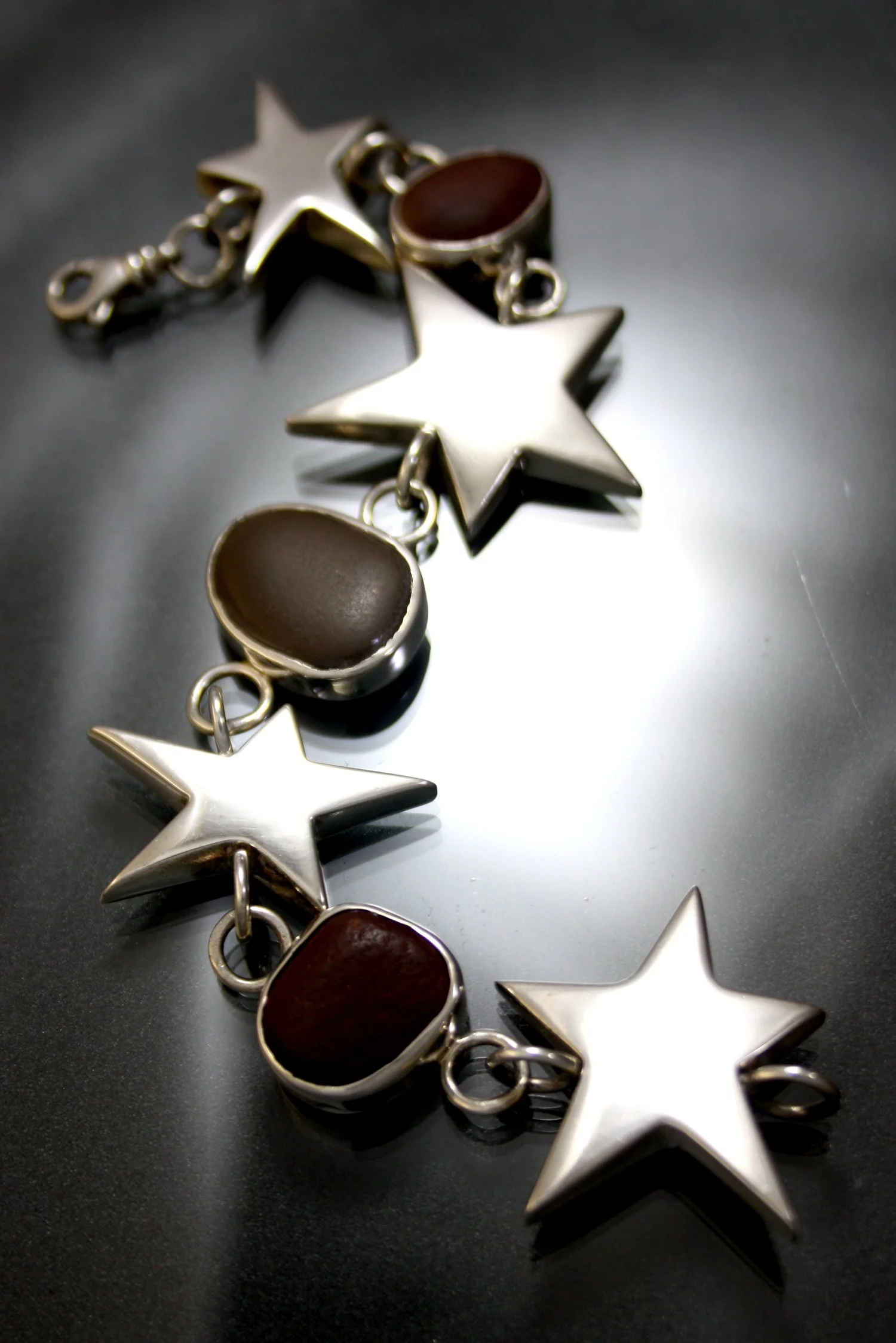 Silver bracelet with star-shaped and oval-shaped charms with dark brown centers, laid on a dark surface.