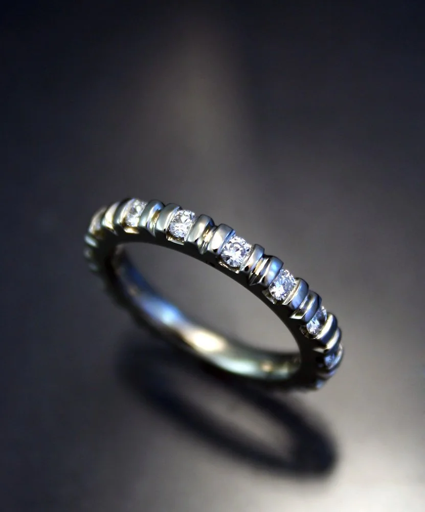 A silver eternity ring with small diamonds set all around, reflecting light against a dark background.