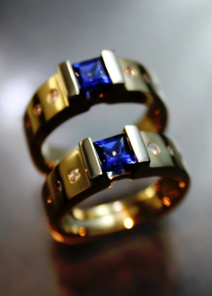 Two gold rings with blue square gemstones and small diamonds on each side of the gemstones.