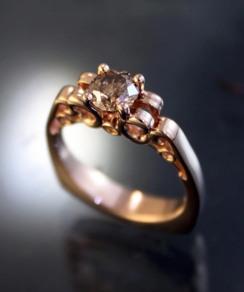 Close-up of a gold ring with a large round-cut diamond in the center and intricate scrollwork designs.