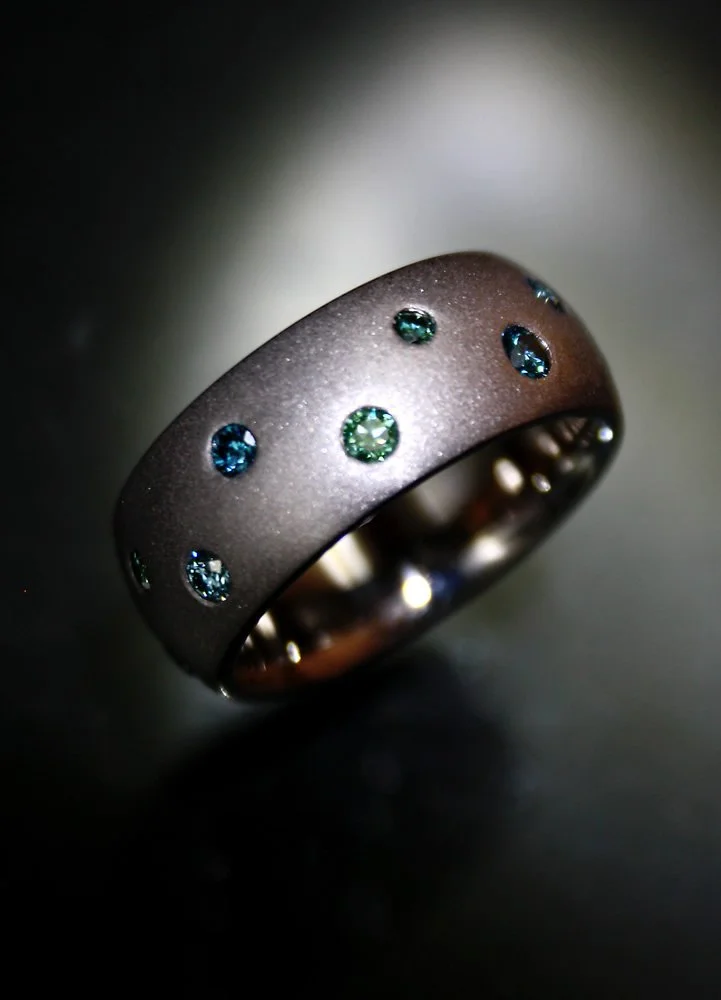 A close-up of a metallic ring with embedded small blue and green gemstones.