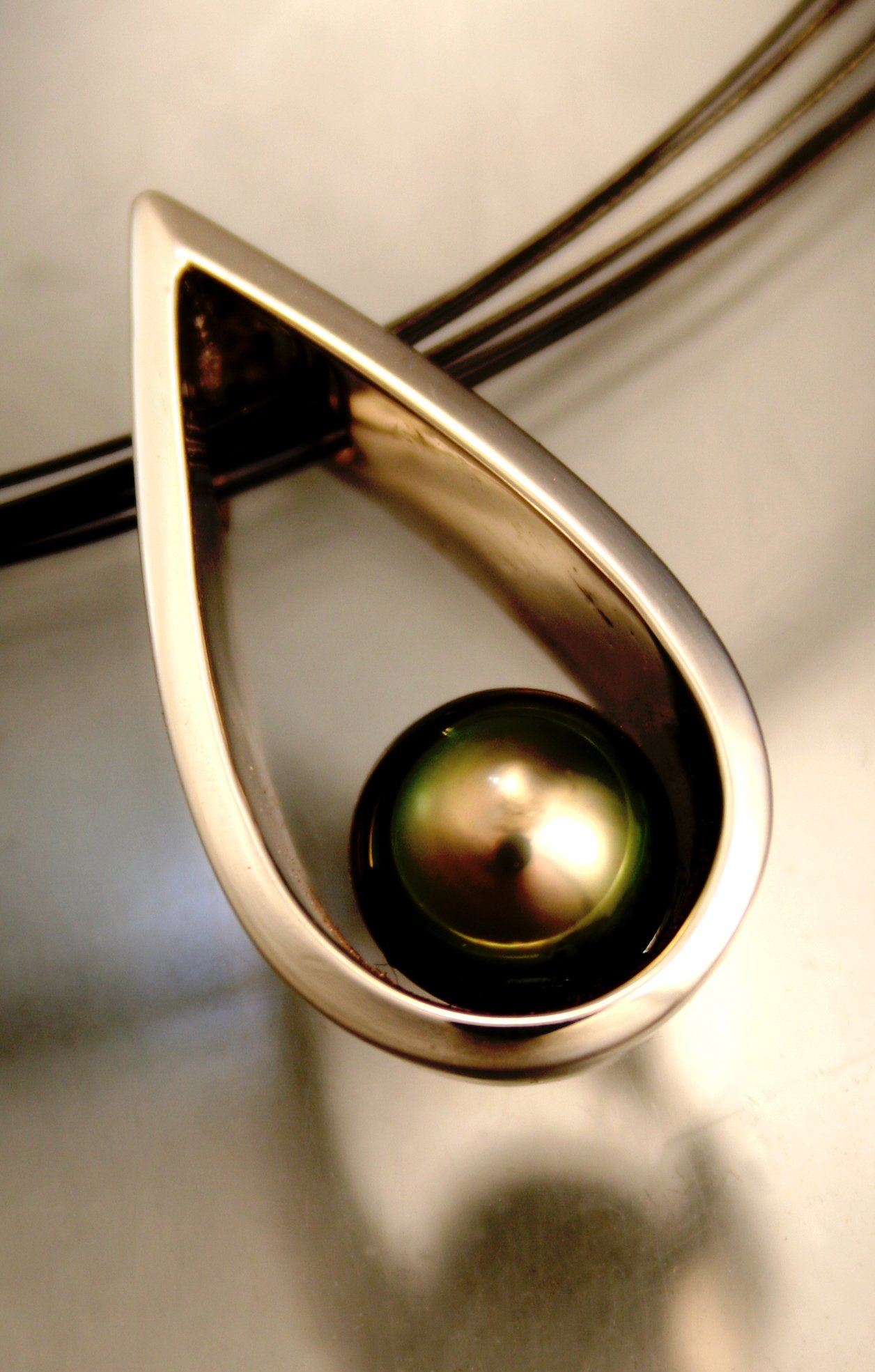 A metallic wall-mounted paper towel dispenser with a silver lid, showing a reflection of the light, and a black bottle with a shiny circular lid inside the dispenser.