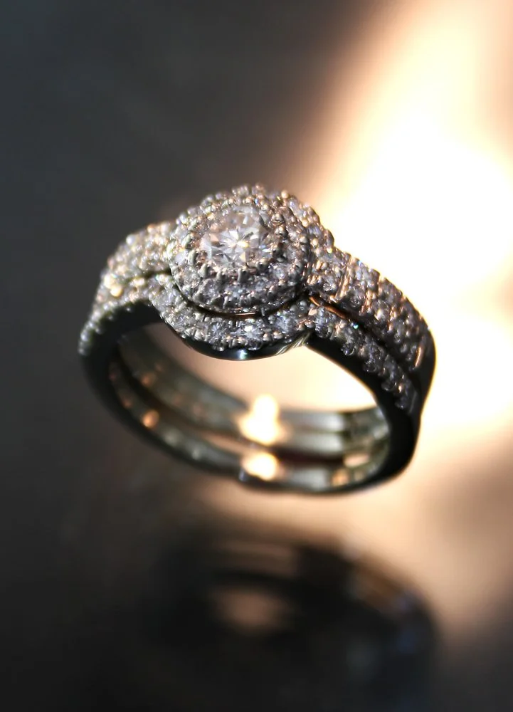 Diamond engagement ring with a round center stone surrounded by smaller diamonds, set on a metallic band and reflecting light.