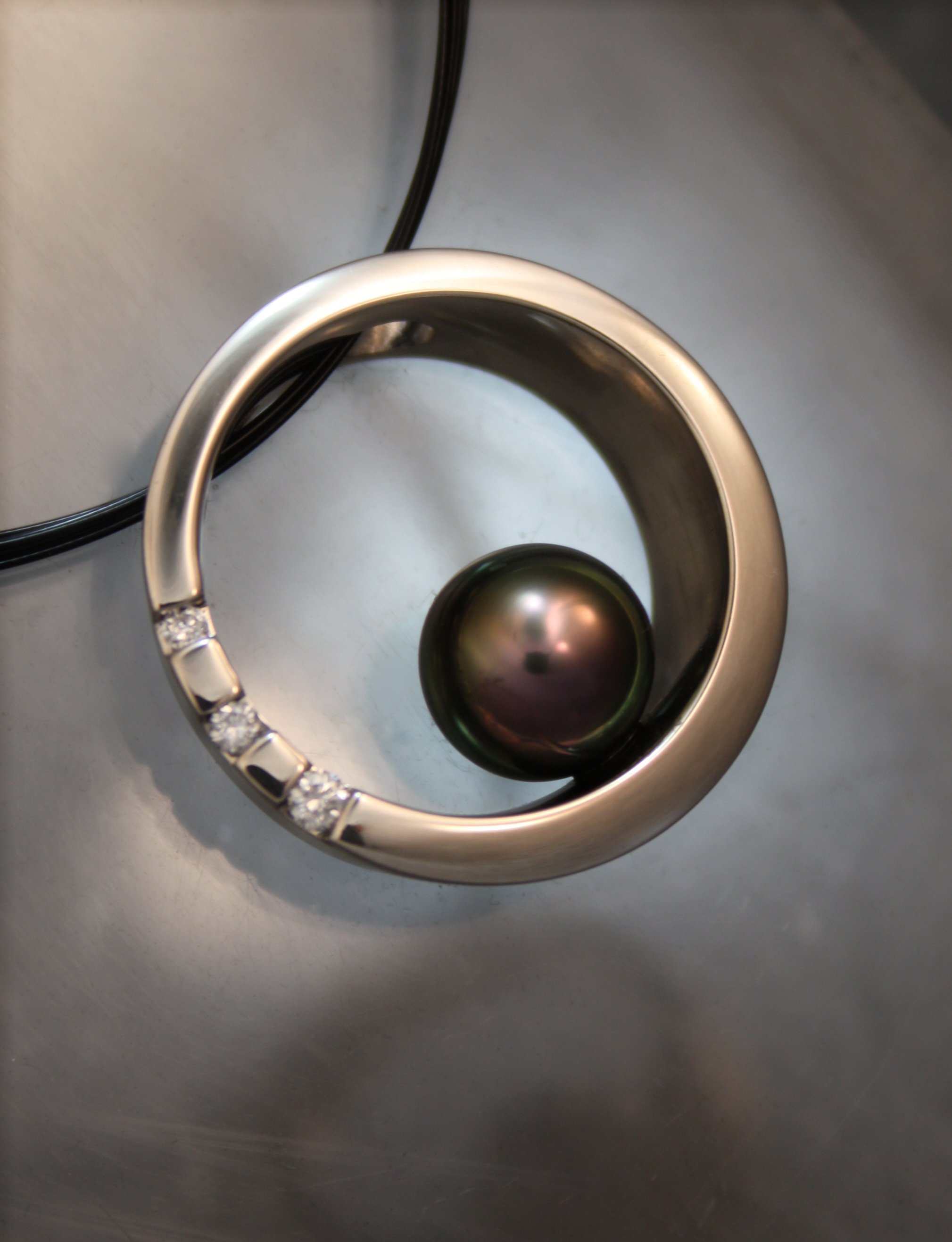 A silver ring with diamonds resting on a reflective black sphere inside a curved metal holder, on a gray surface.