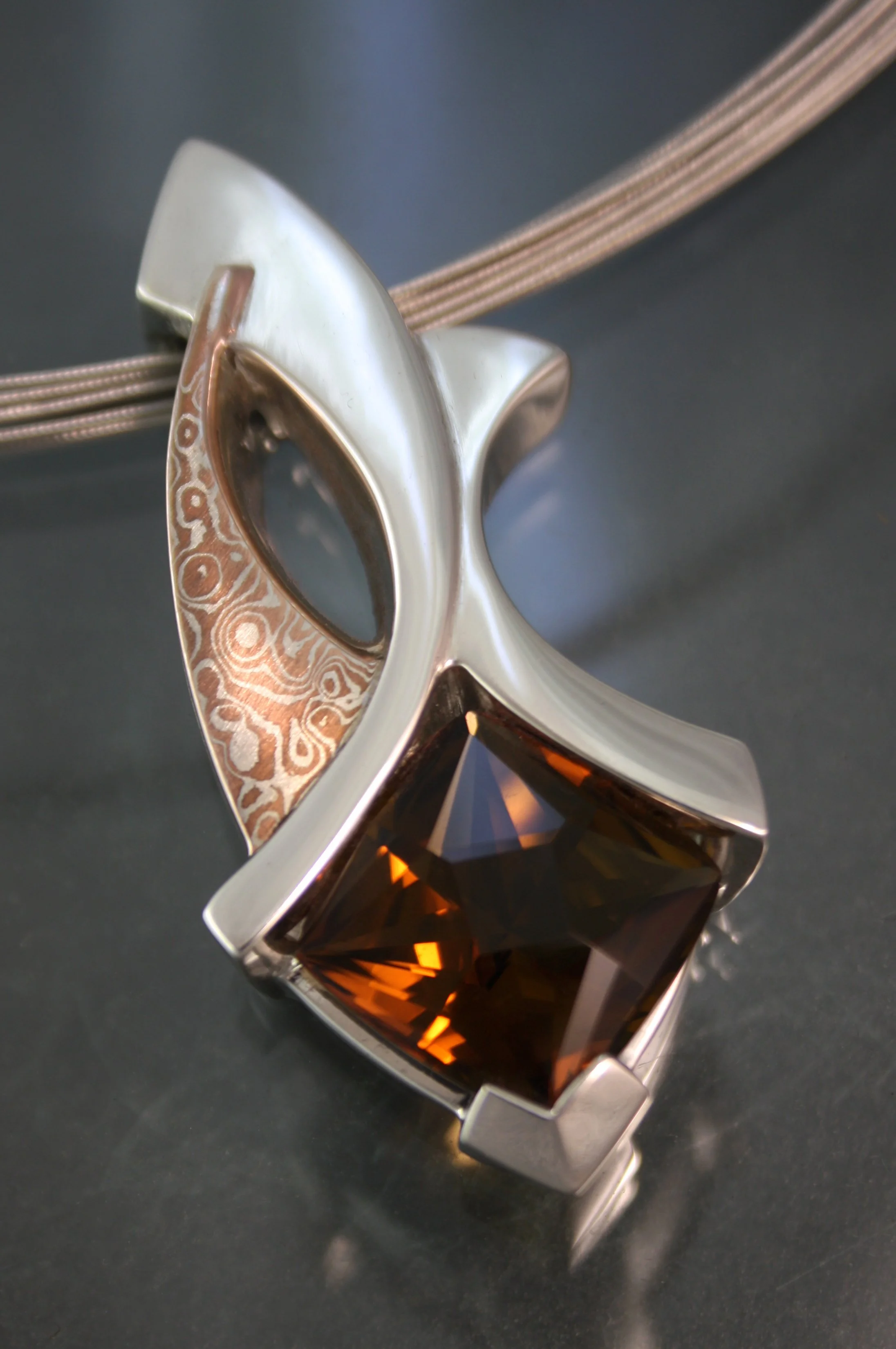 A silver necklace with a large, square, amber-colored gemstone and a decorative, patterned metal piece.
