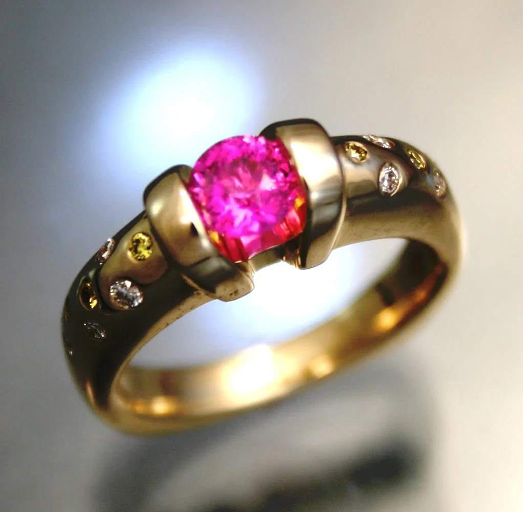 Gold ring with a pink gemstone center and small clear gemstones embedded around it, close-up shot.
