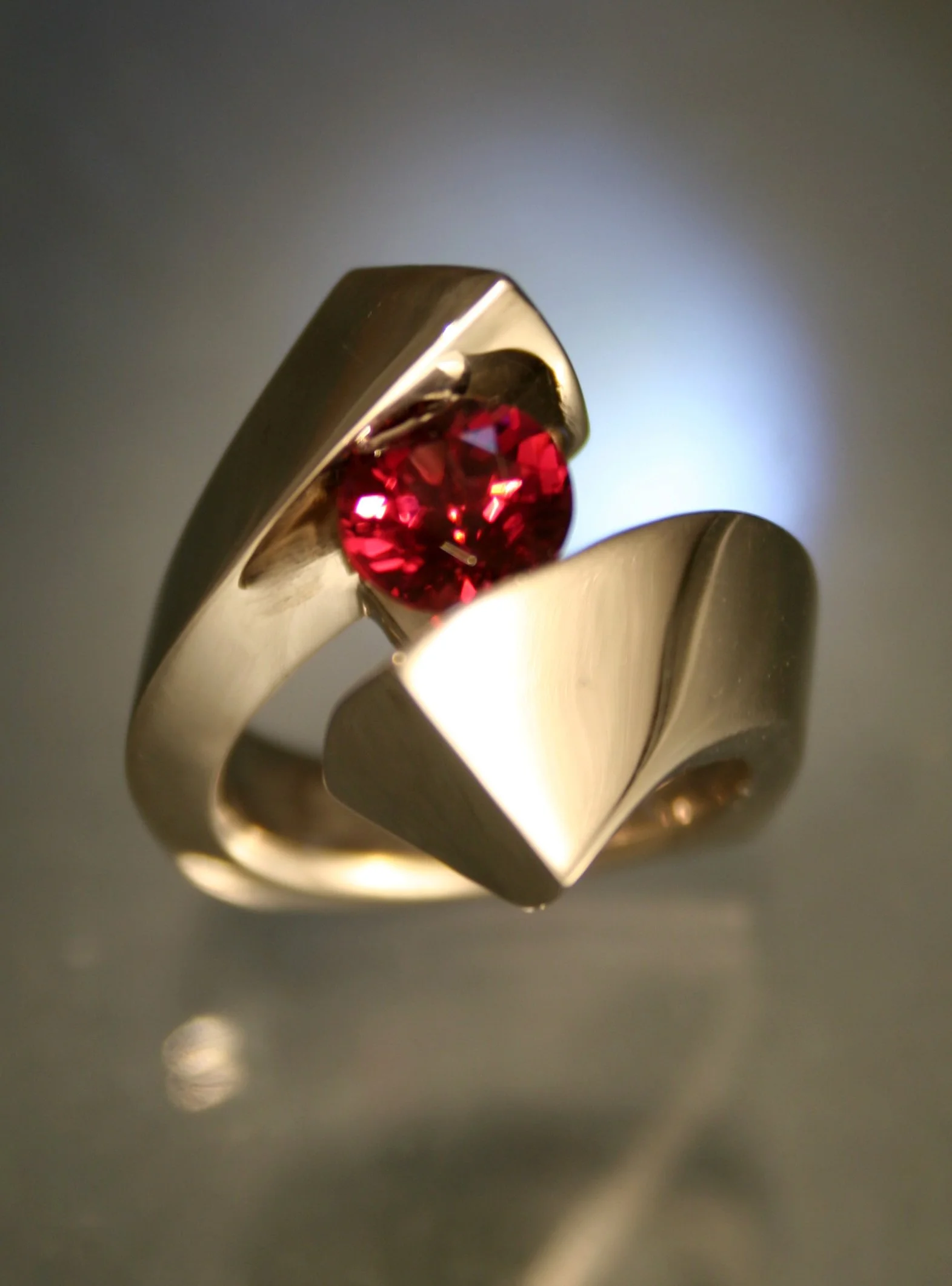 A silver ring with a red gemstone set in the center, featuring a modern, geometric design.
