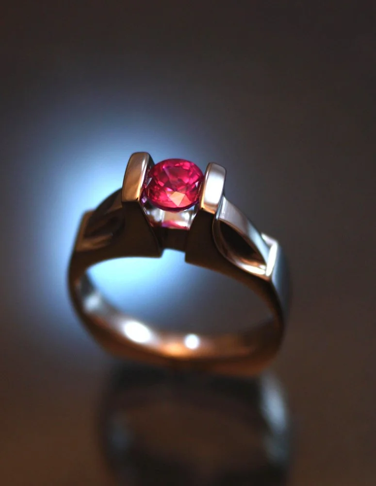 A silver ring with a pink gemstone set in a modern, geometric design, glowing under soft lighting.