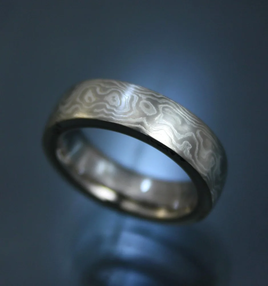 Close-up of a silver ring with a damask pattern, illuminated against a dark background.