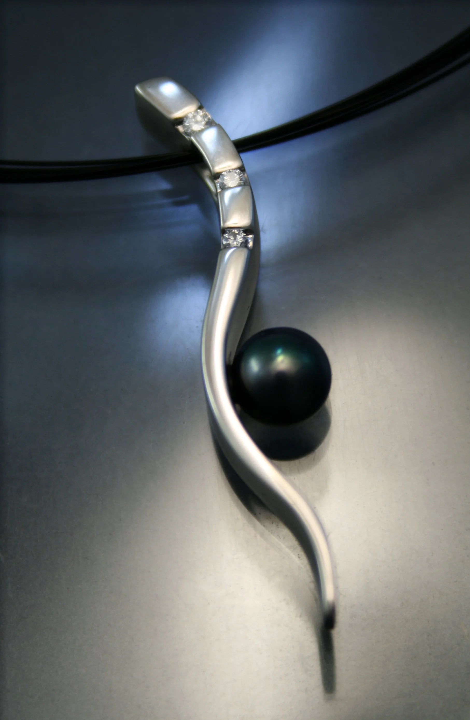 Close-up of a modern jewelry piece with a curved silver design, embedded with small diamonds, positioned on a black sphere, against a dark reflective background.