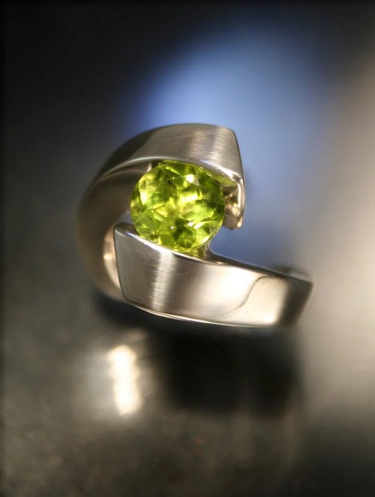 A silver ring with a green gemstone set in the center, with a modern, open design.