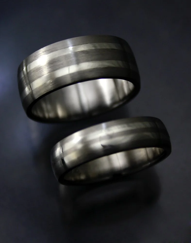 Two metallic rings with black accents, resting on a dark surface, reflecting light.