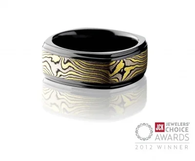 Gold and black patterned ring with a metallic finish and a black interior, displayed against a white background.