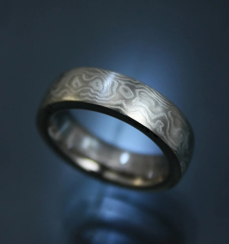 Close-up of a metallic ring with a patterned texture, illuminated in a dark setting.