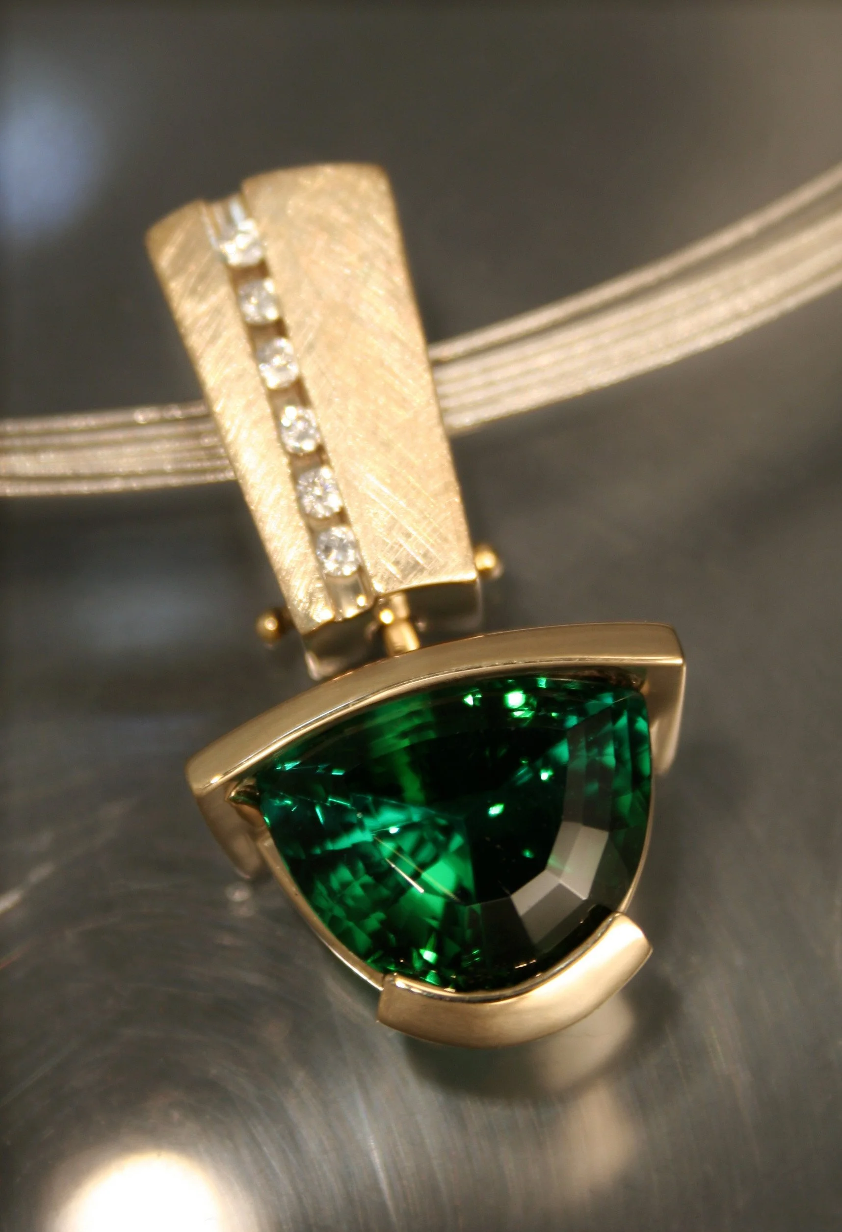 Close-up of a gold pendant with a large green gemstone and a vertical row of small diamonds, hanging from a silver chain.