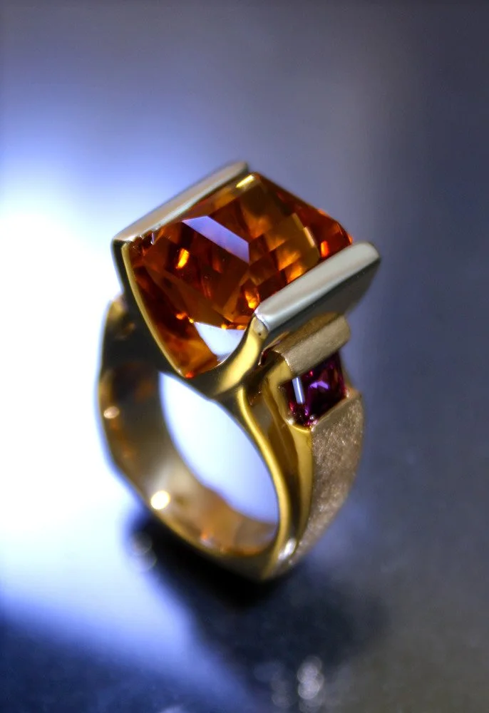 Gold ring with a large rectangular orange gemstone and a smaller rectangular pink gemstone set on the band