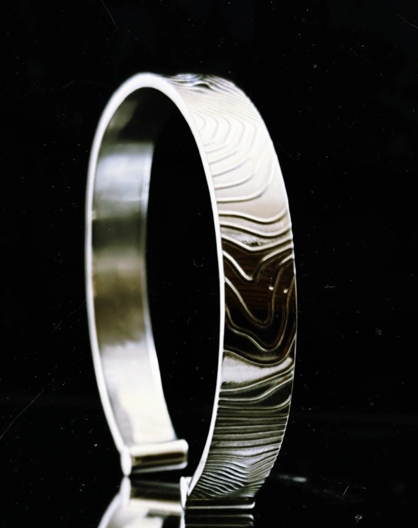 A silver wedding band with a textured, swirled pattern on the outer surface, photographed against a black background.
