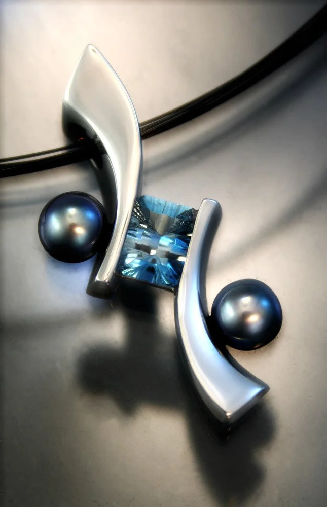 Decorative metal sculpture with curved silver pieces, two dark metallic spheres, and a blue gem in the center placed on a flat gray surface.