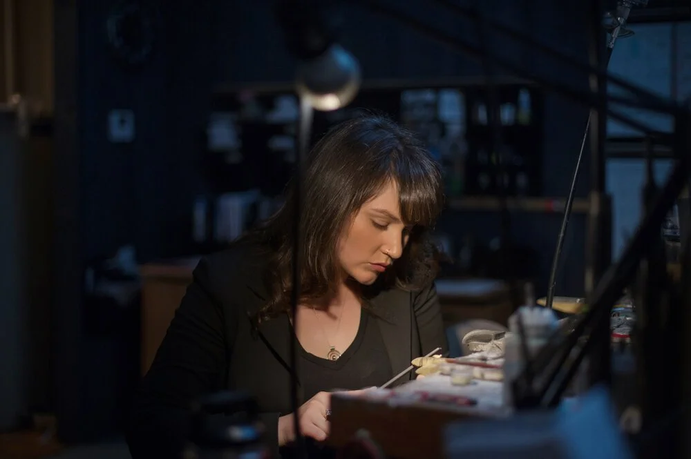 A woman working on an art project at a desk in a dimly lit room.