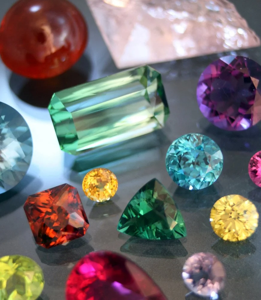 Collection of colorful gemstones and a red apple on a reflective surface.