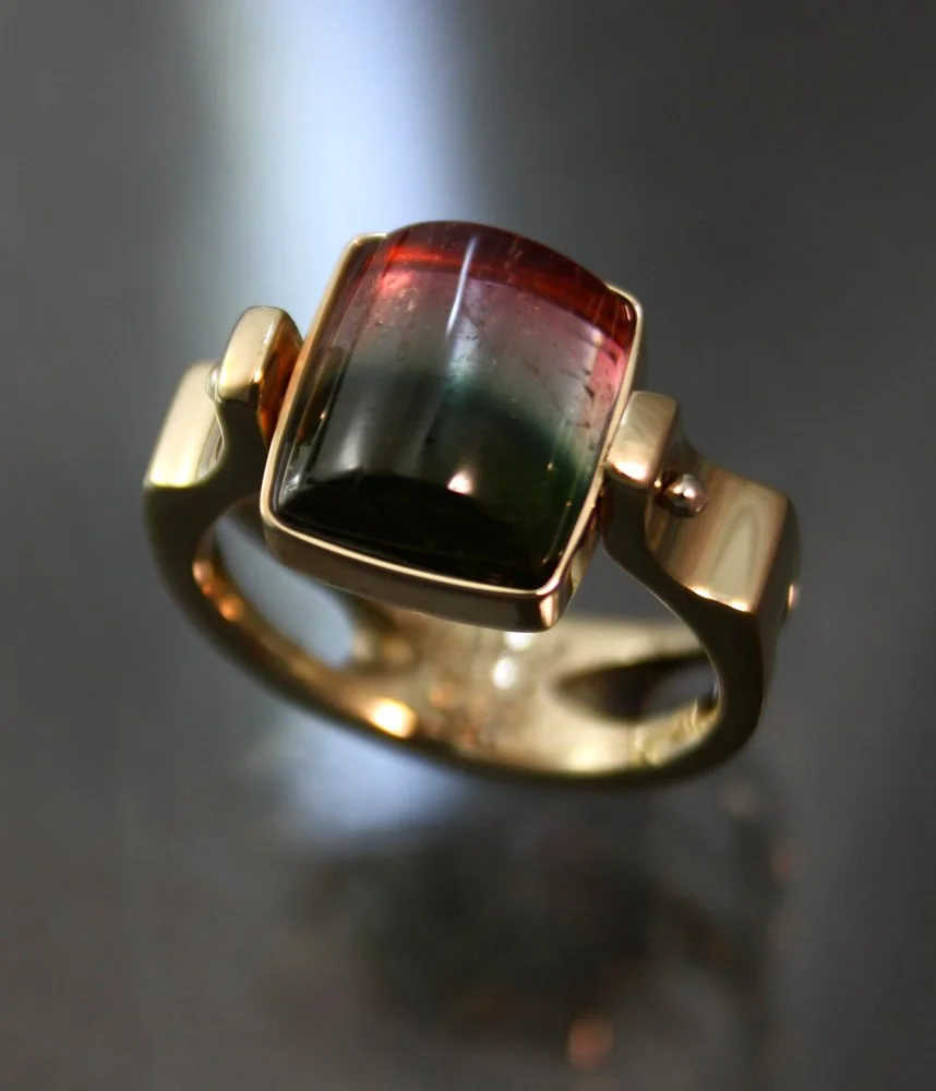 Gold ring with a rectangular black, red, and green gemstone.