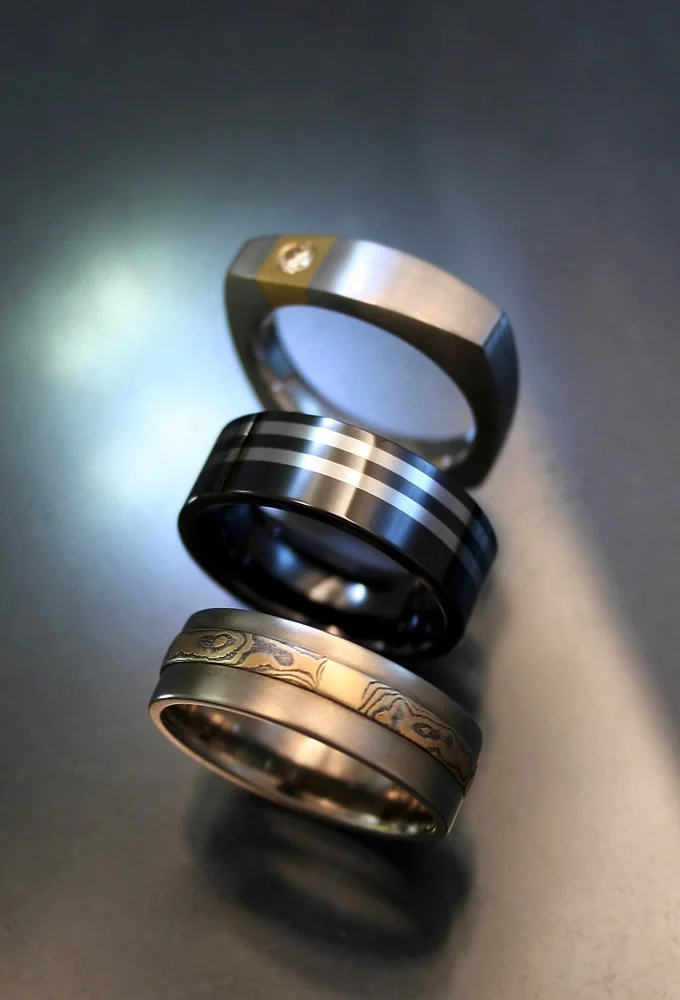 Three men's wedding bands with distinct designs on a dark surface.