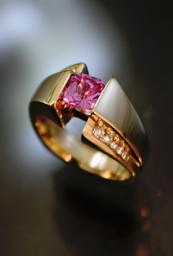 A gold ring with a pink gemstone and small diamonds on a dark surface.