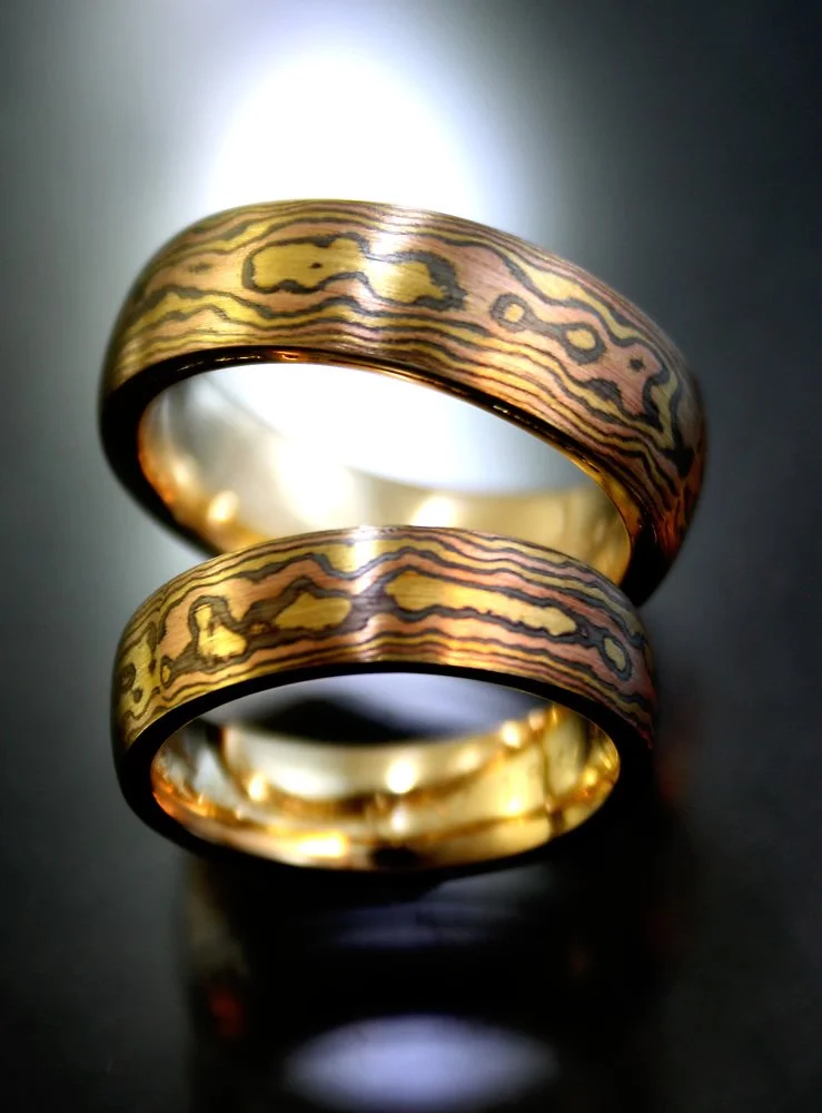 Two gold rings with patterned inlays, overlapping on a dark surface.