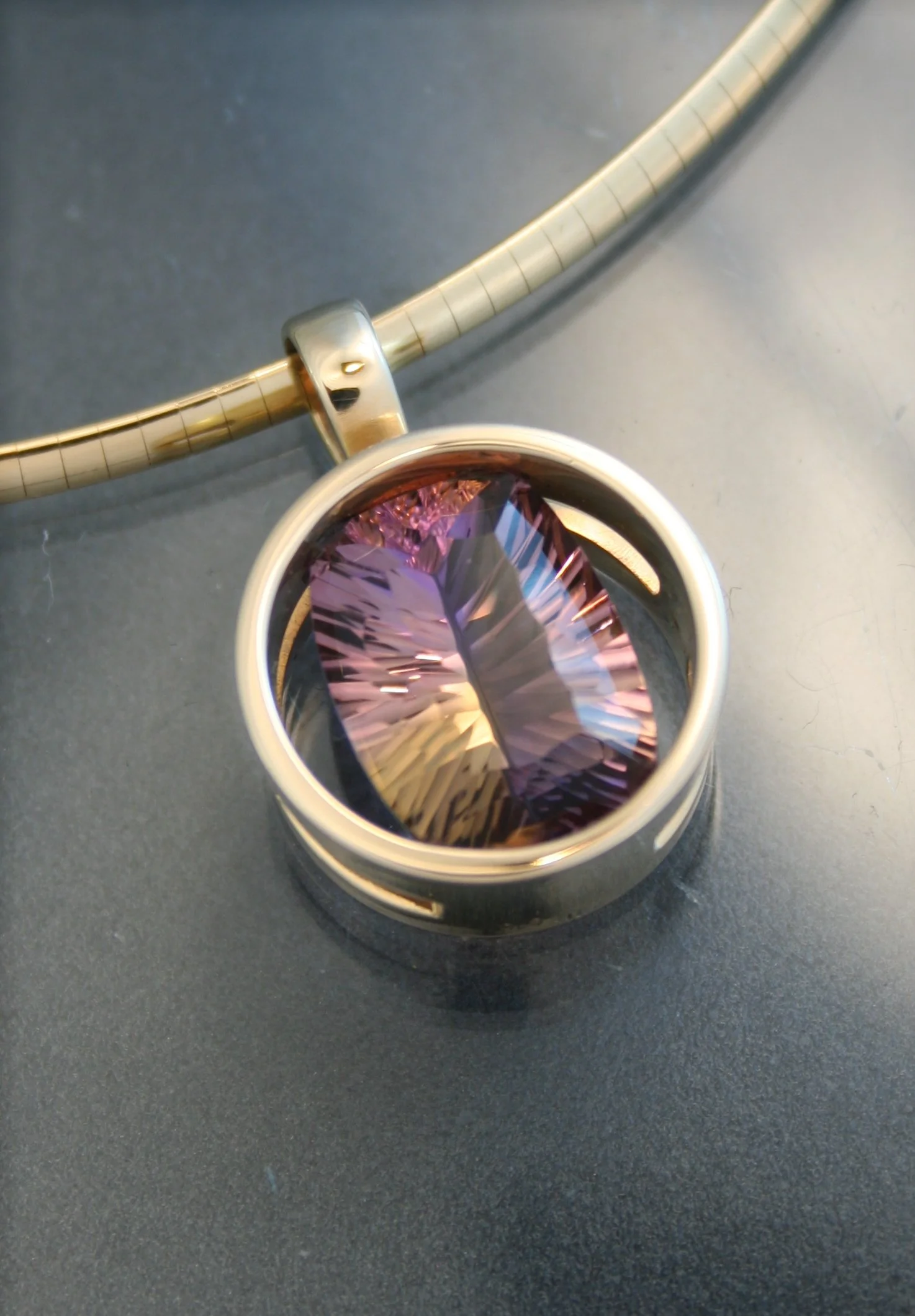 A silver ring with a large, oval, purple gemstone on a black surface with a metallic bracelet in the background.