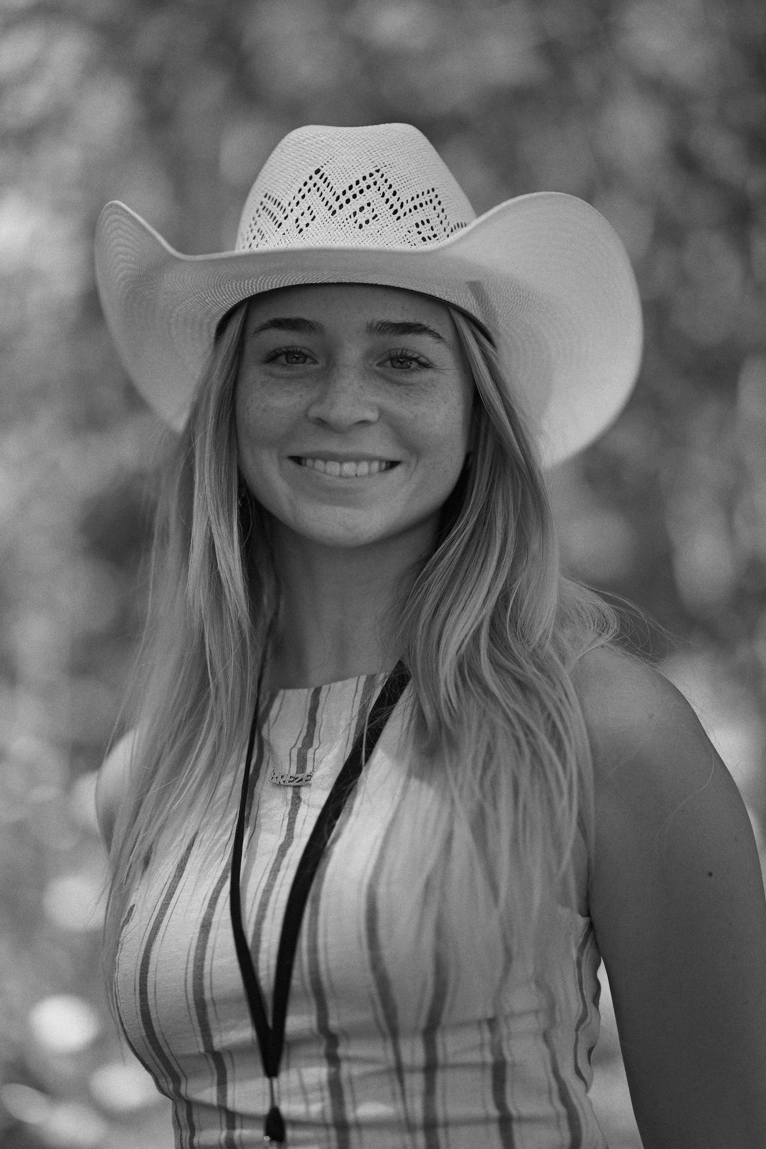 A smiling woman wearing a wide-brimmed hat and a sleeveless striped shirt with a lanyard around her neck.