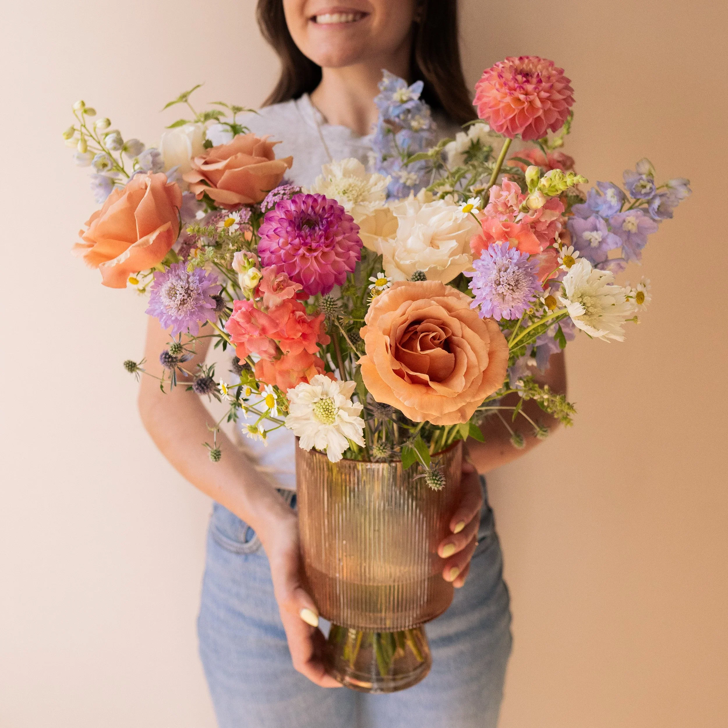 Person holding a large bouquet of colorful flowers in a copper-colored vase.