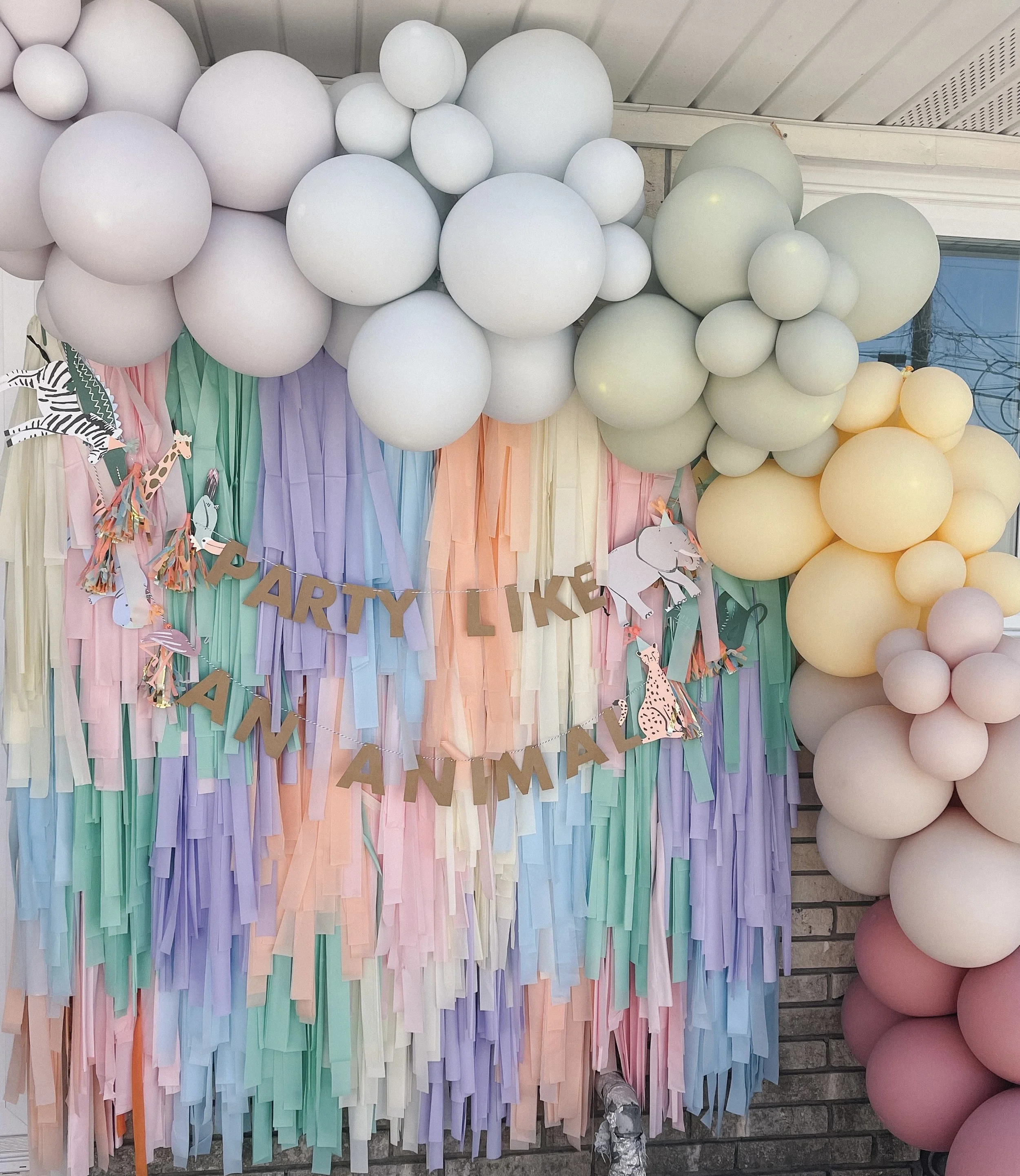 Colorful pastel streamer backdrop with balloons and a banner that reads 'PARTY LIKE AN ANIMAL' for a celebration.