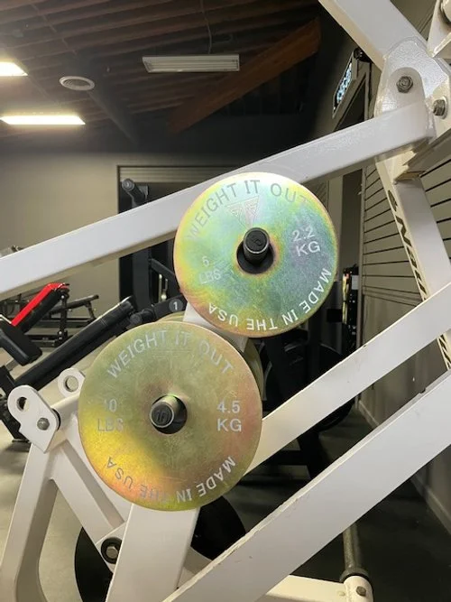 Close-up of two weight plates on a gym machine, labeled 'Weight It Out,' with one plate measuring 2.2 kg (5 lbs) and the other 4.5 kg (10 lbs).