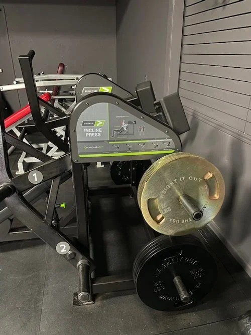 Incline press weight machine with weight plates stacked beside it at a gym.
