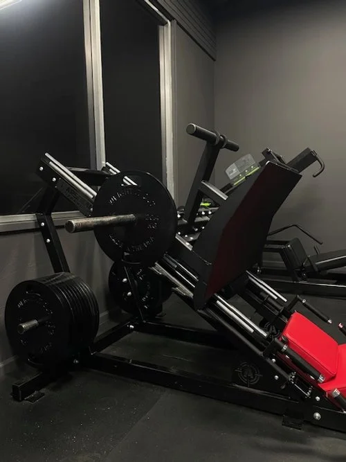 An inclined leg press machine in a gym with black weights on the side.