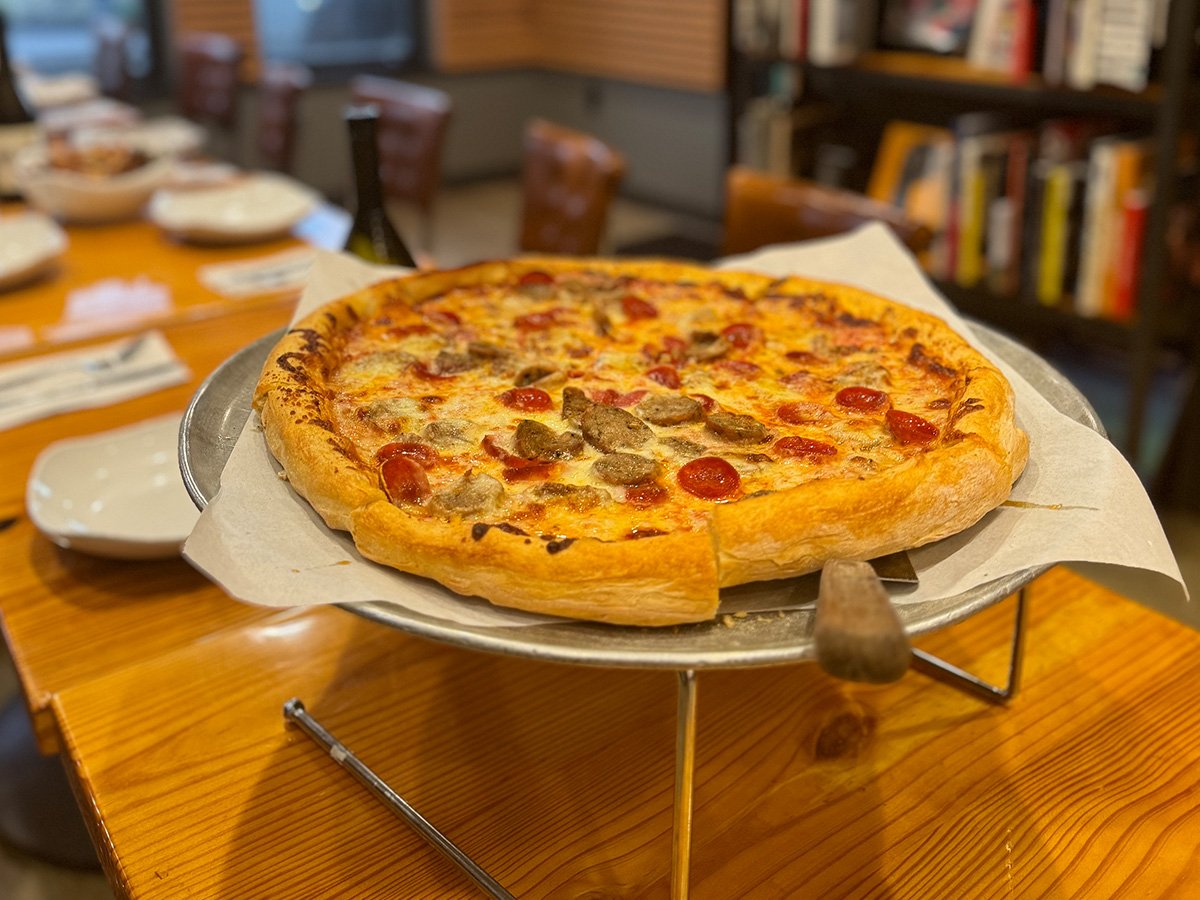 Cheese and pepperoni pizza with sausage on a metal tray on a wooden table in a restaurant.