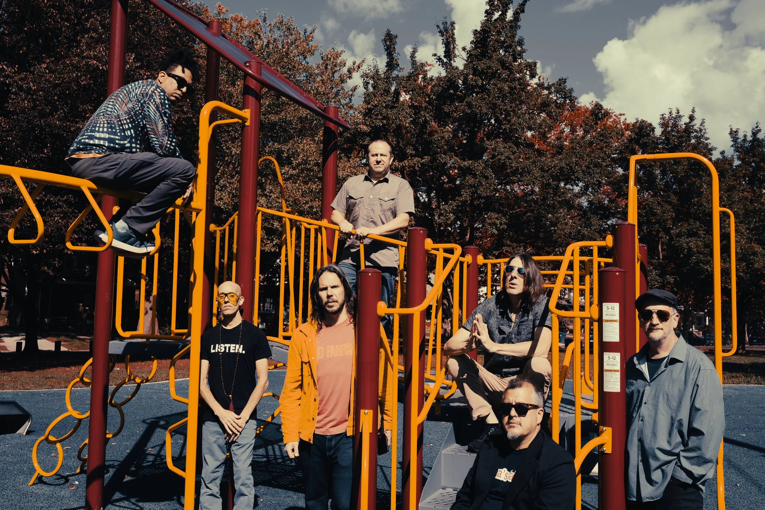 Seven members of band sitting on yellow and red jungle gym