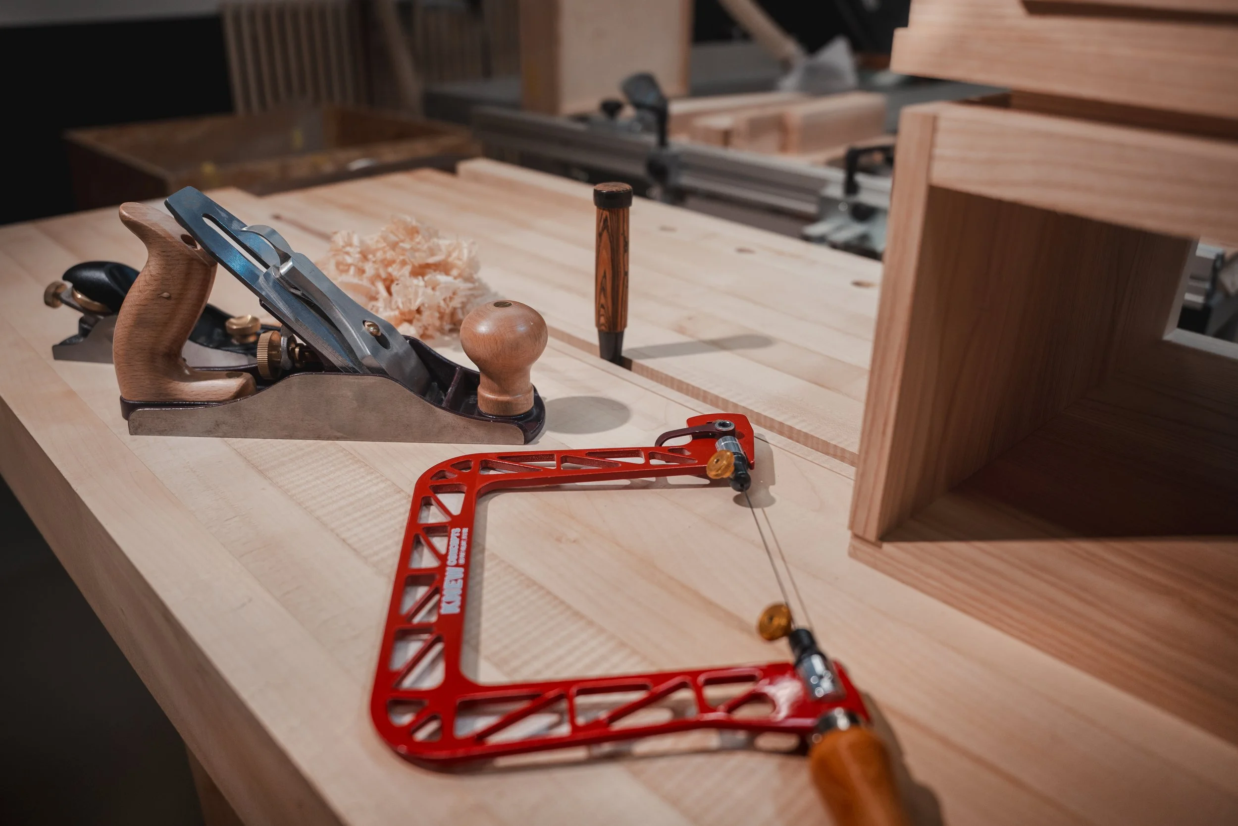 Holzarbeiter-Werkzeug-Set auf einem Holztisch in einer Werkstatt, inklusive Handhobel, Bleistift, Schraubzwinge, Zaun und Holzstücken.