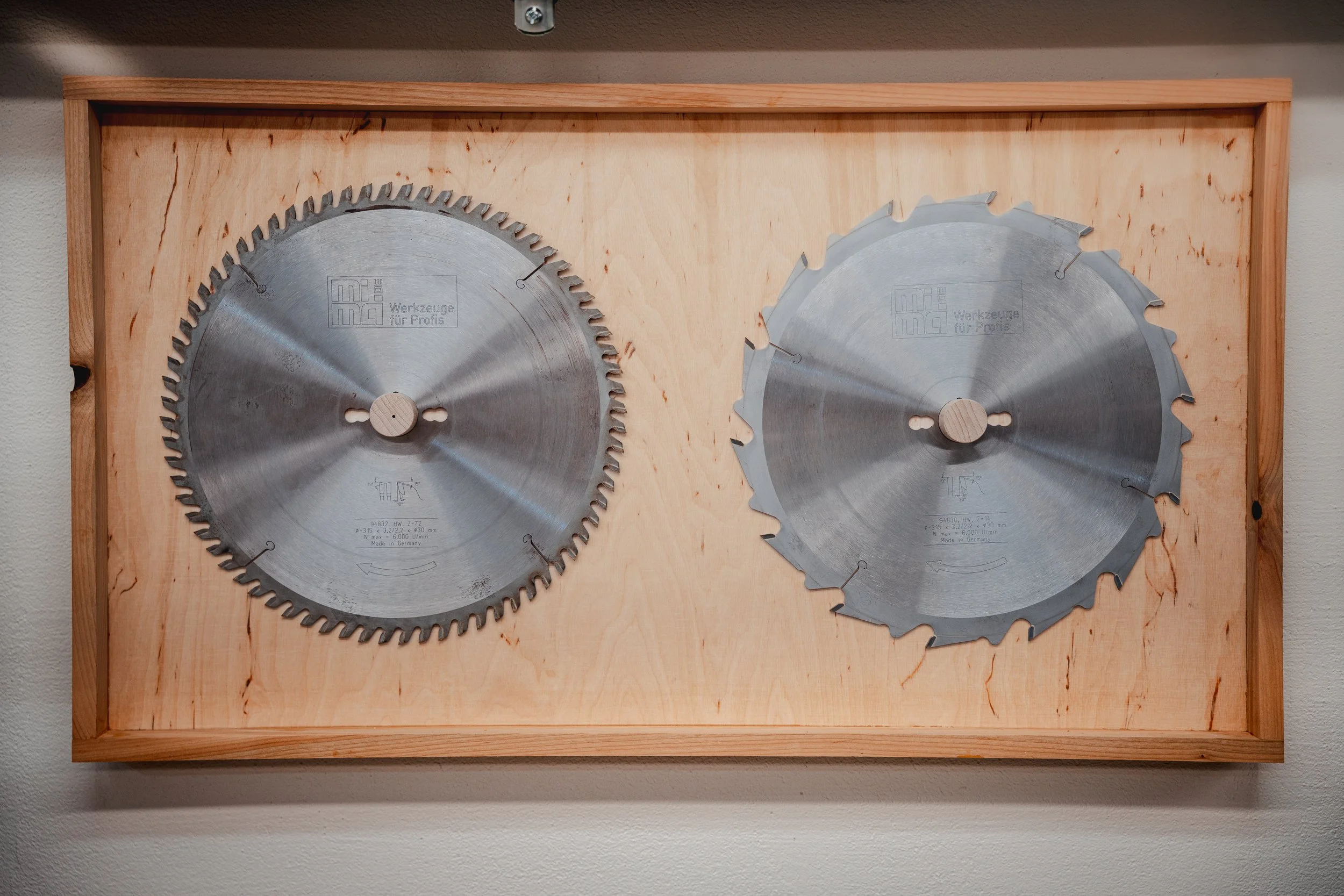 Zwei Kreissägeblätter, eines mit mehr Zähnen, in einem Holzkasten