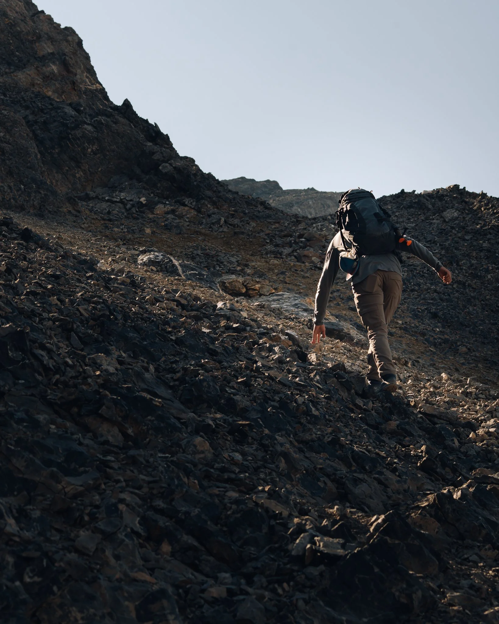 Hiker climbing a rocky mountain trail with a large backpack, steep incline.