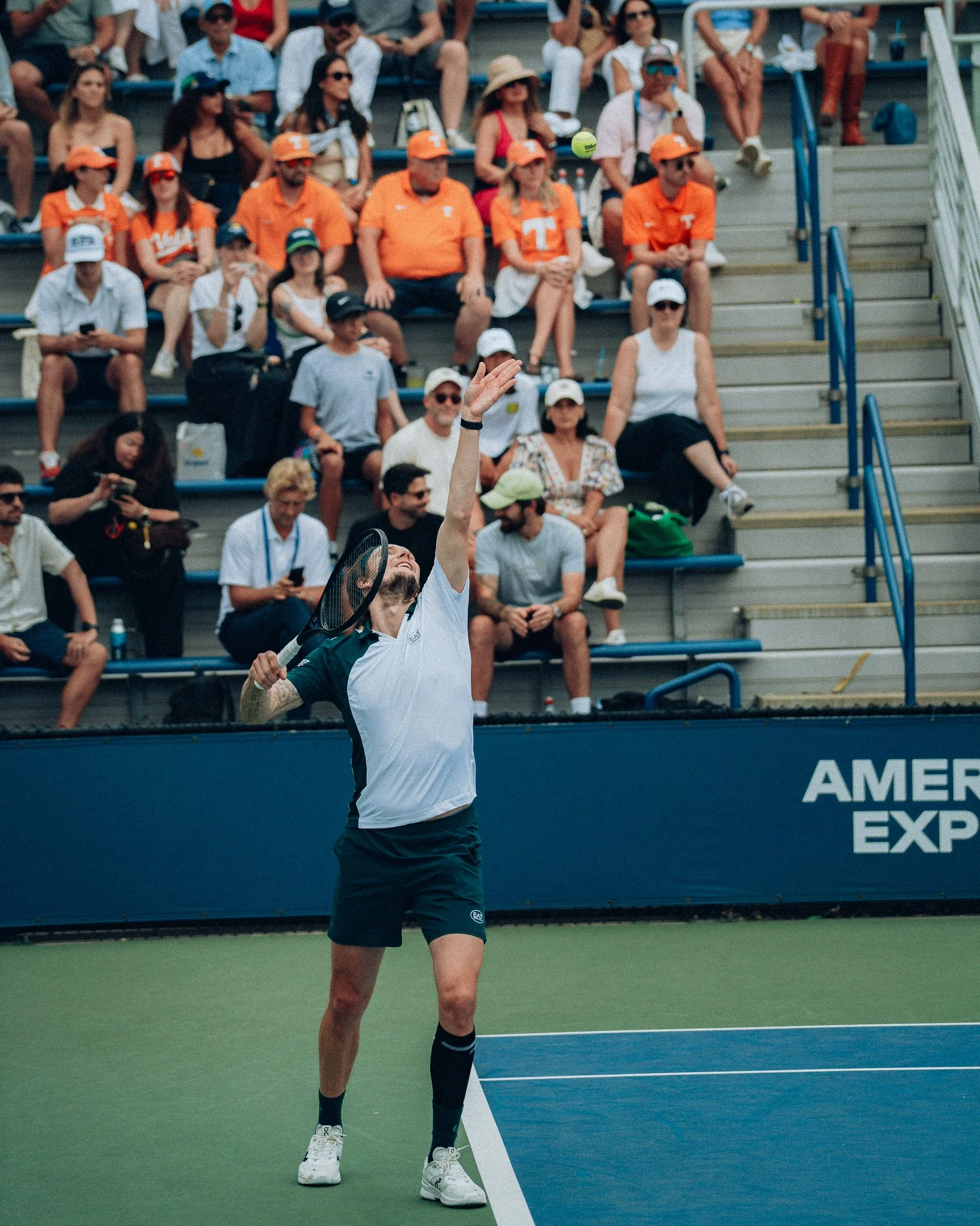 U.S. Open tennis player preparing to serve on a hard court with a crowd of spectators watching from the bleachers in the background.