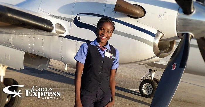 A smiling female airline crew member in uniform standing in front of a small private jet at an airport.