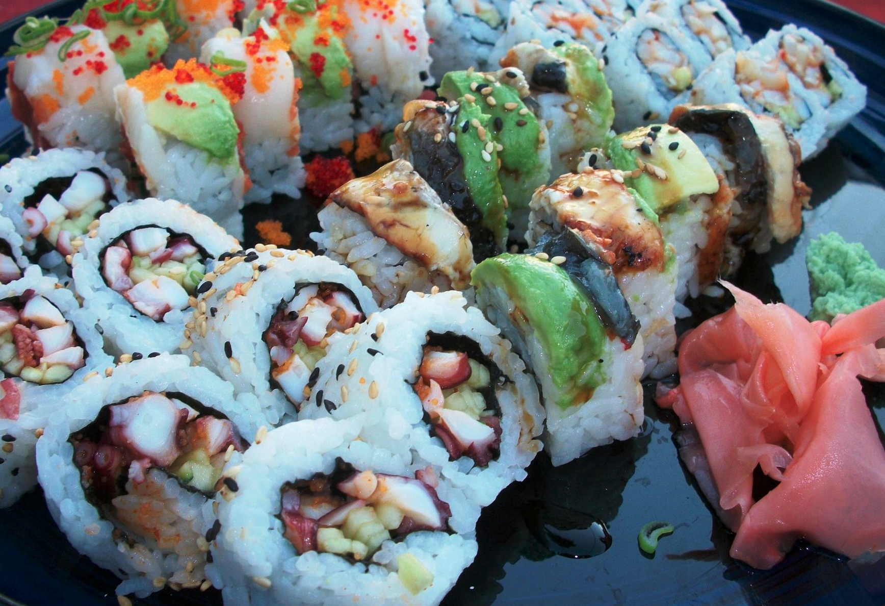 An assortment of sushi rolls with various ingredients, topped with fish, avocado, and sesame seeds, served with pickled ginger and wasabi.