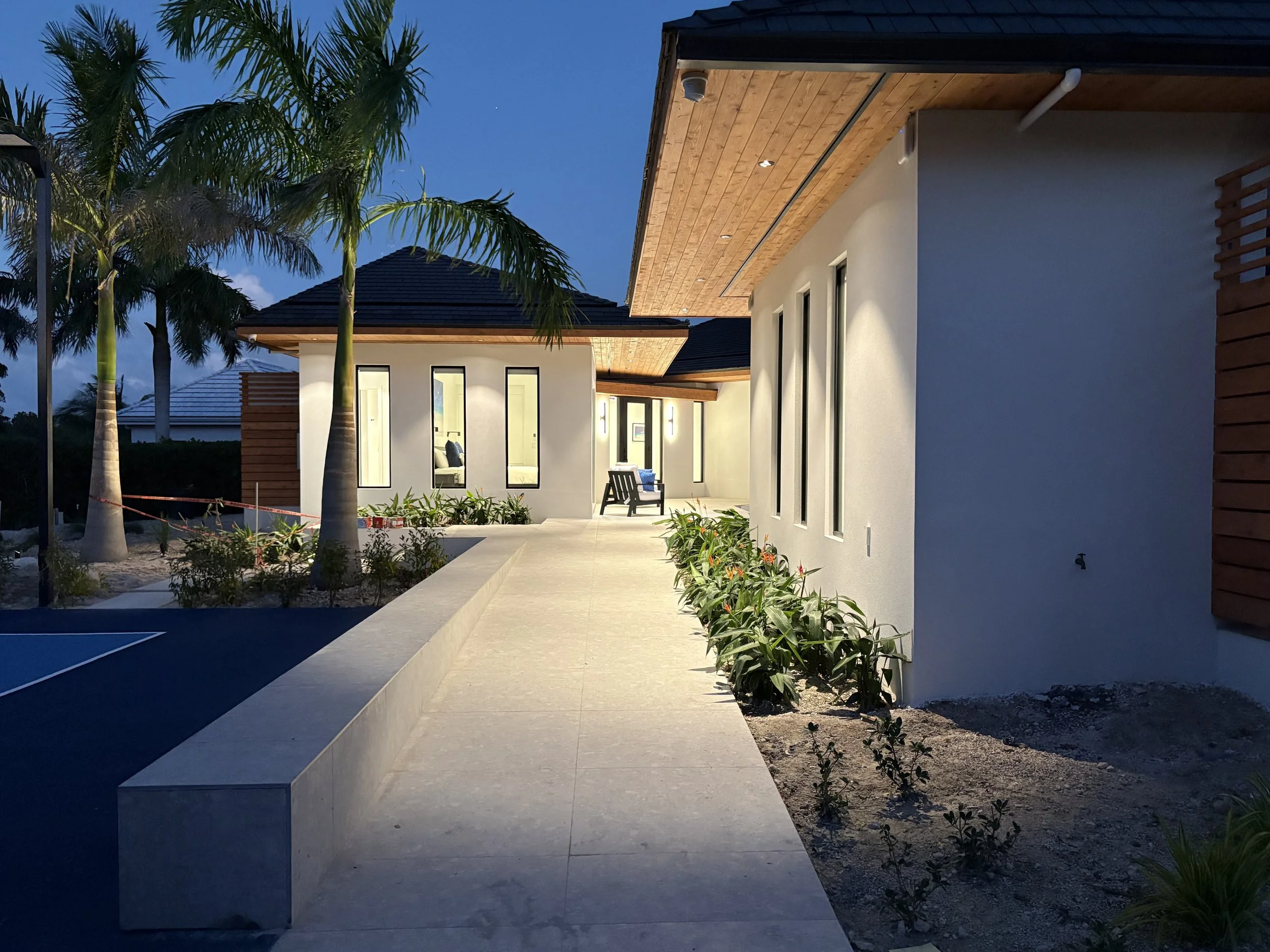 Modern house exterior with pathway, palm trees, and outdoor seating area during twilight