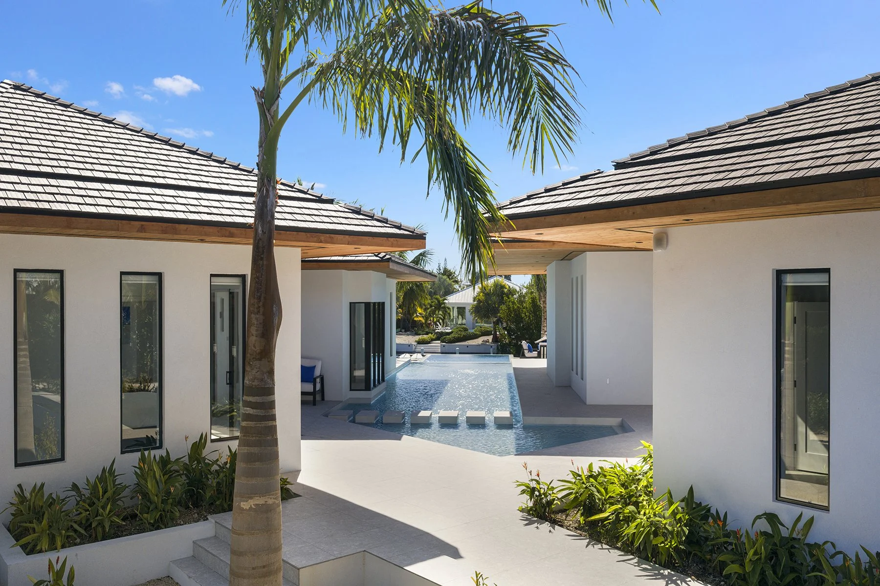 View of a modern backyard with a pool, palm trees, and contemporary white buildings under a clear blue sky.